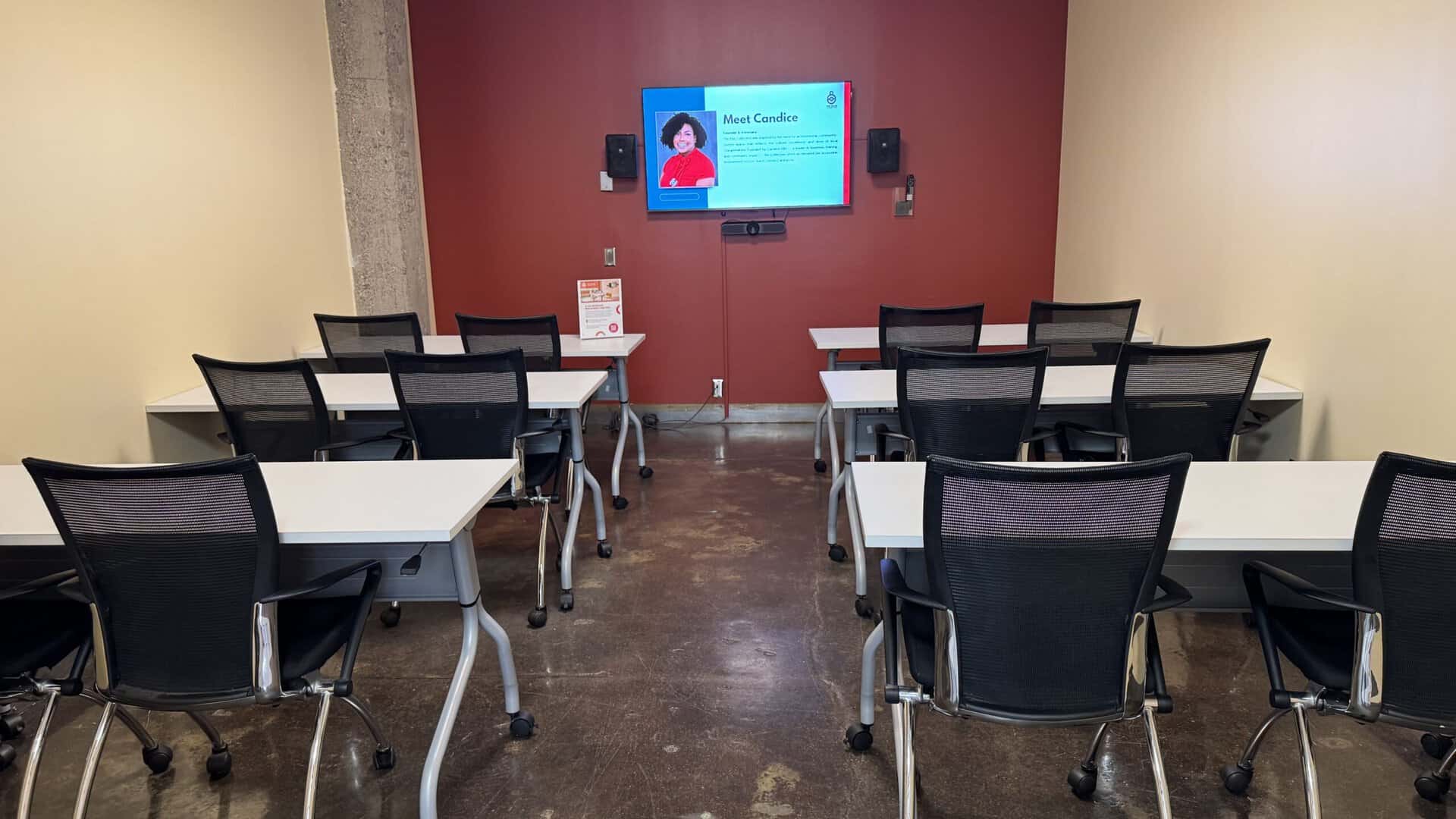 picture of a training room with tables and chairs pointed at a video screen